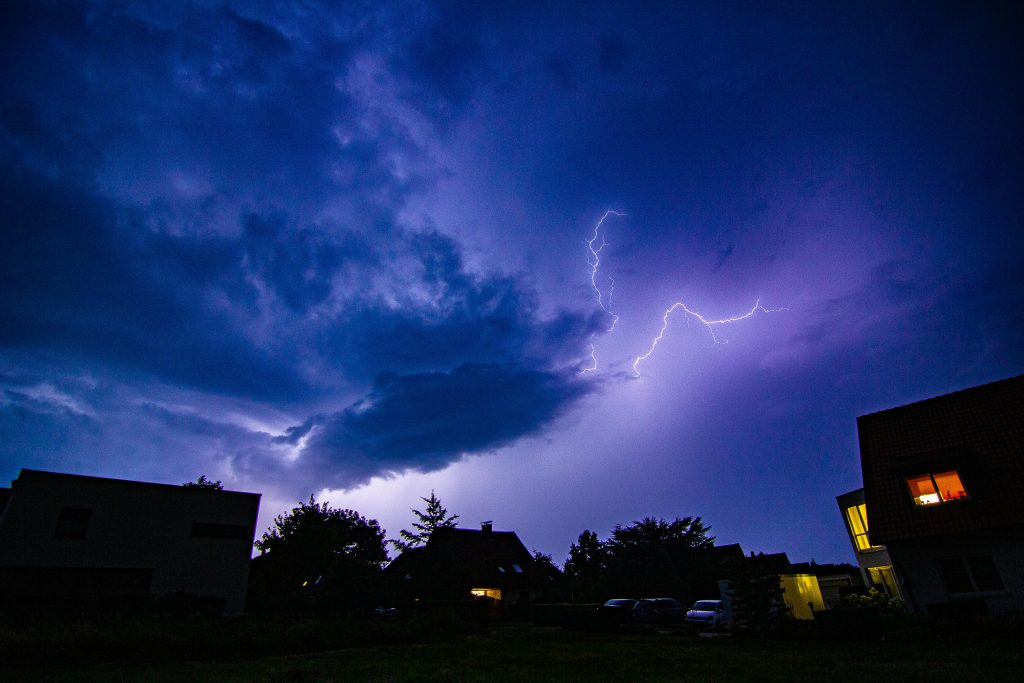 A striking nighttime scene capturing vivid lightning and dark clouds over silhouetted suburban houses.