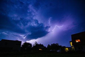 A striking nighttime scene capturing vivid lightning and dark clouds over silhouetted suburban houses.