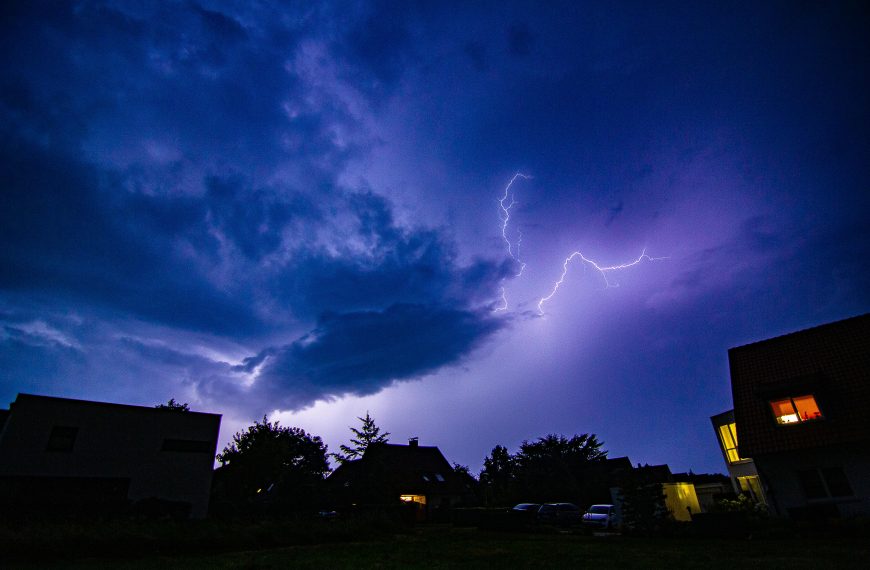 A striking nighttime scene capturing vivid lightning and dark clouds over silhouetted suburban houses.